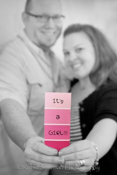 a man and woman holding up a pink card that says it's a girl