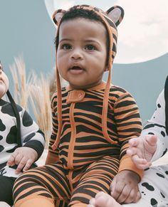 two babies dressed in animal print outfits sitting next to each other, one baby wearing a tiger costume