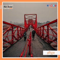 two people walking across a red bridge with orange railings on either side and an orange sign that says har dwar