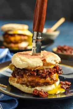 a sandwich on a plate with a knife stuck in the meat and cheese buns