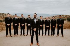 a group of men standing next to each other in front of a desert area with mountains