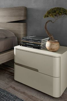 a small bonsai tree on top of a white nightstand next to a gray bed