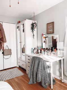 a bedroom with white furniture and lots of items on the table in front of it