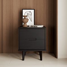 a small black cabinet with a vase on top in a room that has wood paneled walls