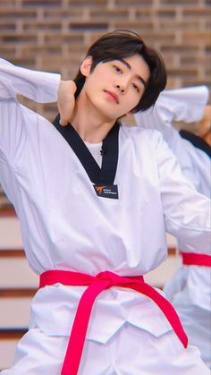 a man in white shirt and red belt standing next to another person with black hair