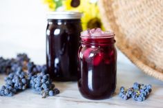 two jars filled with blueberries next to some flowers