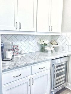 a kitchen with white cabinets and marble counter tops