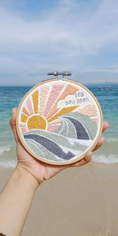 someone is holding up a cross stitched sun and ocean scene with the words, sea you soon