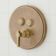 a brass colored faucet with three knobs and two handles on a white tile wall