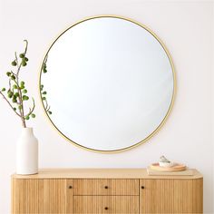 a round mirror sitting on top of a wooden dresser next to a vase with a plant