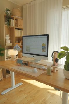 a computer monitor sitting on top of a wooden desk next to a potted plant