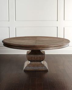 a round wooden table on a hard wood floor in front of a white paneled wall