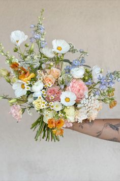 a woman holding a bouquet of flowers in her hand with tattoos on it's arm