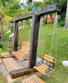 a wooden swing with chains hanging from it's sides in the grass near some palm trees