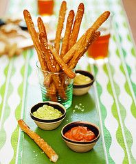 homemade pretzel sticks with three mustards in small bowls on a green and white tablecloth