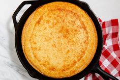 a cast iron skillet sitting on top of a white marble counter next to a red and white checkered napkin