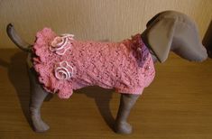 a dog wearing a pink sweater with flowers on it's collar and tail, standing in front of a wall