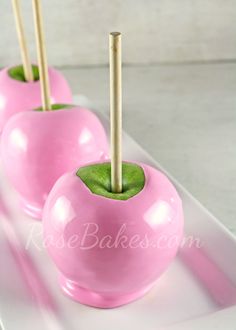 three pink apples with wooden sticks sticking out of them on a white plate, ready to be eaten