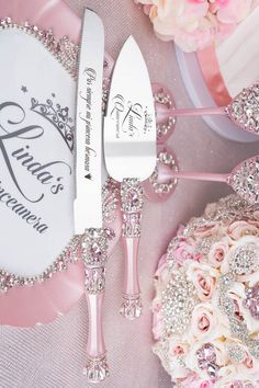 a table topped with pink flowers and silverware next to a white plate covered in crystal