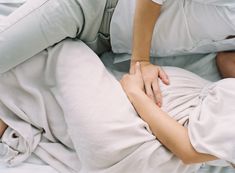 a woman laying on top of a bed covered in white sheets and pillows holding her hands together