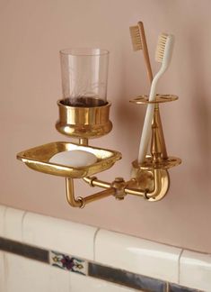 two toothbrushes and a cup on a gold plate in a bathroom wall holder