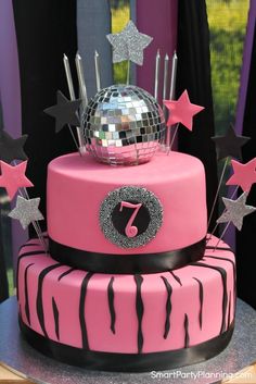 a pink cake with black and white designs on it's sides is topped with a disco ball and stars