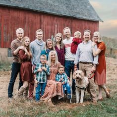 a large family poses for a photo in front of a red barn with their dog