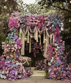 an outdoor ceremony with flowers and tassels hanging from it's sides, surrounded by greenery