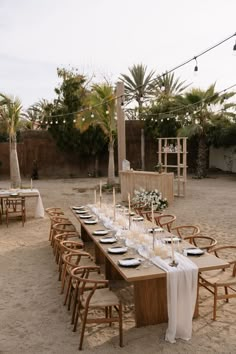 a table set up with white linens and place settings for dinner on the beach