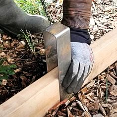 a pair of work gloves on top of a piece of wood next to a person's foot