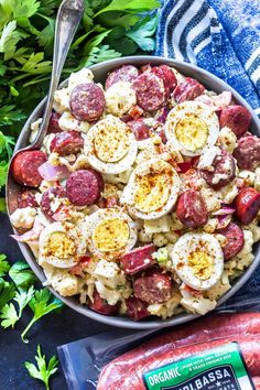 a bowl filled with pasta, eggs and sausage next to a bag of potato salad