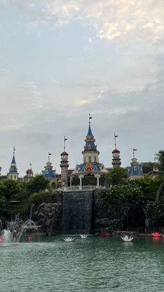 an amusement park with water and fountains in the foreground, surrounded by greenery