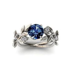 a blue diamond ring with leaves and diamonds on the band, set in white gold