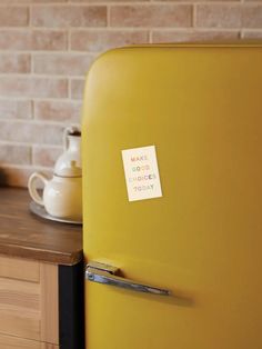 a yellow refrigerator with a sticker on it sitting in front of a brick wall