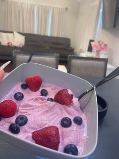 a bowl of ice cream with strawberries and blueberries in it on a table