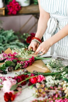 a woman arranging flowers on a table in front of other floral arrangements and greenery