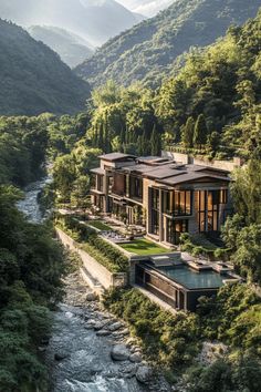 an aerial view of a house in the mountains with a river running between it and trees