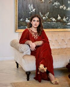 a woman is sitting on a couch in front of a painting and wearing a red dress