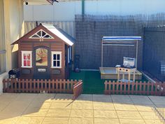 a small wooden house sitting on top of a patio next to a green lawn and fence