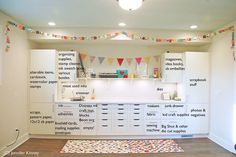 a kitchen with lots of white cabinets and colorful flags hanging from the ceiling above it