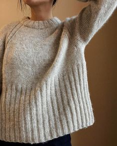 a woman is wearing a sweater and holding her hair in the air with one hand