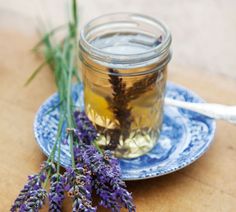 lavender flowers sit on a plate next to a jar of honey and spoons with liquid in it