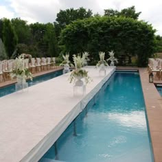 an outdoor wedding setup with chairs and flowers on the edge of the pool, surrounded by greenery