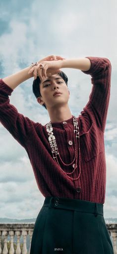 a young man in a red sweater and black skirt is posing for a photo with his hands on his head