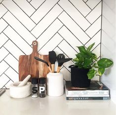 kitchen utensils and wooden cutting board on white countertop next to potted plant