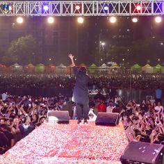 a man standing on top of a stage with his arms in the air while people watch