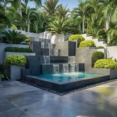 an outdoor fountain surrounded by trees and plants in the middle of a courtyard area with concrete steps leading up to it