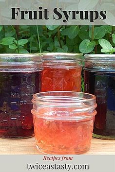 four jars filled with fruit syrups sitting on top of a wooden table next to plants