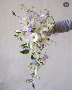 a bouquet of white and purple flowers is being held by someone's hand in front of a wall