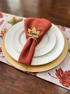 a place setting with napkins, plates and an autumn maple leaf on the napkin